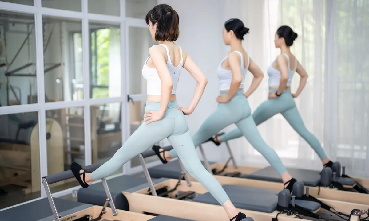 Drie vrouwen in nauwsluitende leggings en sporttopjes doen een uitvalspas op een rij reformers