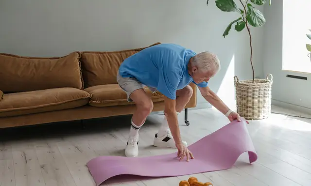 Oudere man rolt thuis in de woonkamer een roze oefenmat uit op een lichte houten vloer